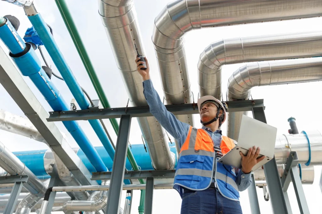 A technician inspecting pipes and industrial installations using a laptop