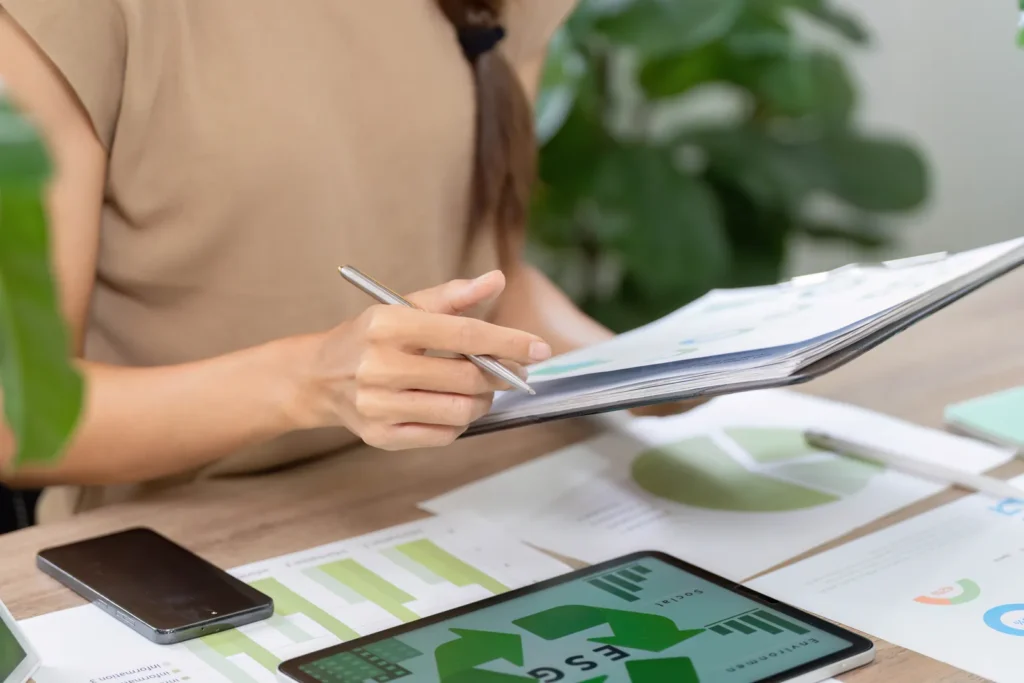 Manos revisando un informe ESG con gráficos de sostenibilidad sobre la mesa